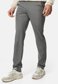 Szare, slim-fit spodnie z gładkiego, lekkiego materiału; posiadają przednie kieszenie oraz płaski przód, zestawione z beżowymi butami sportowymi.