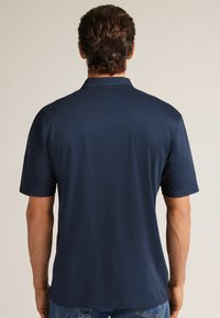 Granatowa koszulka polo z krótkim rękawem, gładki wzór, miękka tkanina, widok z tyłu pokazujący kołnierzyk oraz brak widocznego tekstu lub logo.