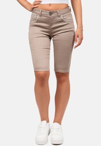 Shorts en denim beige à coupe slim, avec des coutures blanches sur les poches et une texture lisse, associés à des baskets blanches.