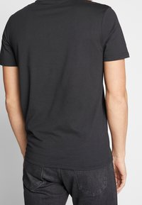 Černé tričko s krátkým rukávem vyrobené z bavlny, s kulatým výstřihem a slim fit střihem, s hladkou texturou a minimálními detaily švů.