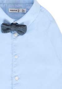 Camicia azzurra chiara con colletto e chiusura a bottoni, con cravatta a farfalla grigia strutturata attaccata al collo. Realizzata in tessuto morbido, ideale per un look casual.