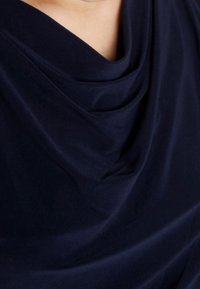 Tela de un azul oscuro drapeada, textura suave con suaves pliegues, mostrando un diseño de escote tipo cowl. Sin patrones ni adornos visibles.