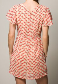 Lyhyet hihaiset, levenevät mekko kevyestä kankaasta, jossa on toistuva kirsikkakuosi punaisena ja vihreänä vaalealla taustalla. V-mallinen kaula-aukko.