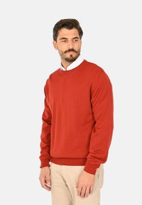 Maglione di cotone rosso con collo rotondo, maniche lunghe e polsini a coste, abbinato a pantaloni beige. Tessuto liscio e vestibilità casual.