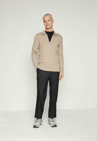 Sweater bege com fecho no pescoço, combinado com calças pretas e sapatilhas cinzas. O tecido parece suave, e o corte é ajustado e moderno.