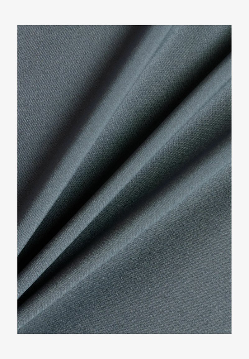 Zacht, soepel grijs stof gevouwen met lichte plooien, toont fijne textuur en matte afwerking in gelijkmatige belichting.