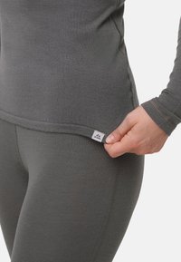 Tummanharmaa pitkähihainen paita ja leggingsit, joissa on sileä pinta, hienovaraiset ompelusaumat ja sivulla oleva logotunniste.