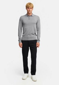 Grå pikétröja med lång ärm, krage, ribbade muddar och fåll, kombinerad med svarta byxor och vita sneakers. Enkel, figurnära design.