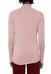 Sweter z długim rękawem w jasnoróżowym kolorze z golfem z prążkowanym kołnierzem, gładką fakturą i zakrzywionym dołem, w połączeniu z czerwonymi spodniami sztruksowymi.