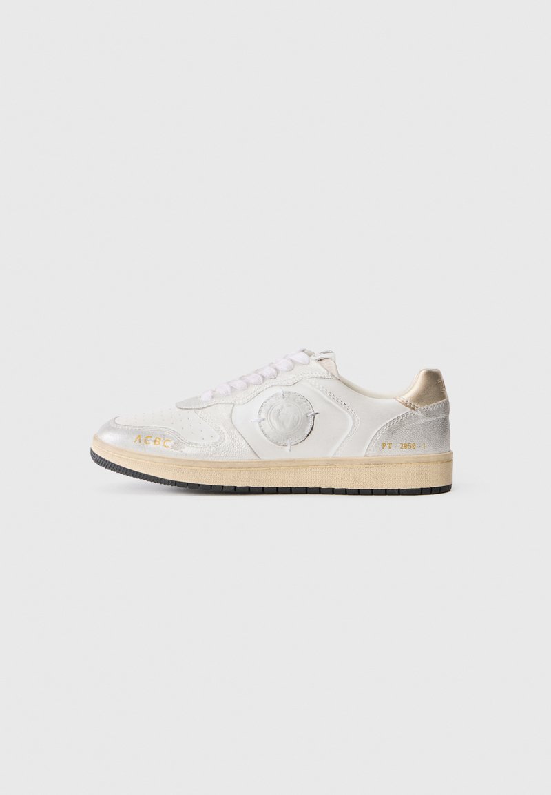Baskets blanches en cuir avec une surface texturée, accents argentés, emblème rond et talon beige clair. Semelle en caoutchouc noire avec inscription dorée.