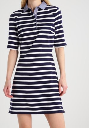 Femme portant une robe polo rayée horizontale bleu marine et blanche avec des manches courtes et un col bleu clair.