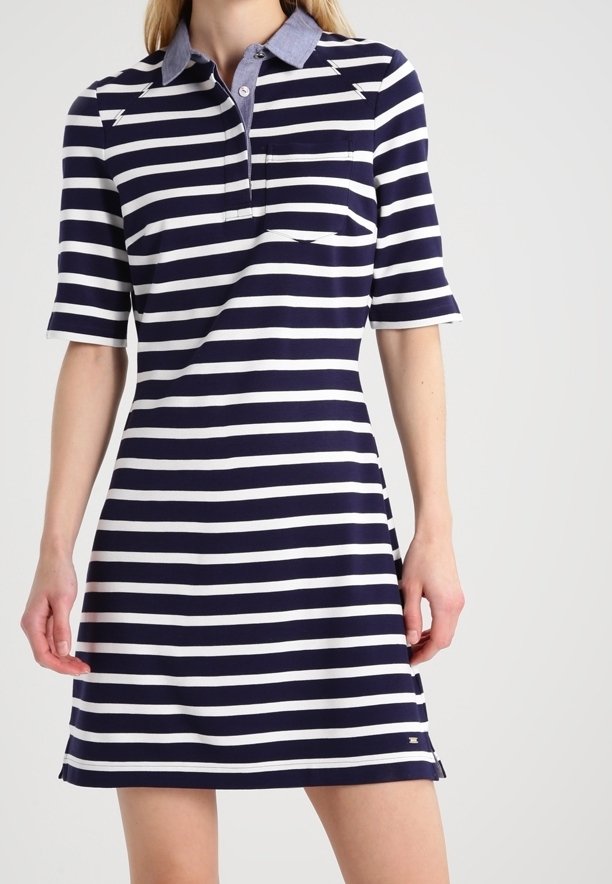 Mujer vestida con un vestido polo de rayas horizontales en azul marino y blanco, con mangas cortas y un collar de color azul claro.