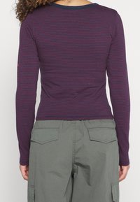 Langarmshirt in dunkellila und burgunder Streifen, mit runder Ausschnitt, figurbetontem Design und leichtem Stoff. Kombiniert mit Cargo-Hosen.