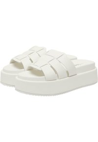 Sandales plates blanches avec de larges brides et une finition mate texturée. Style slip-on avec une semelle épaisse et rembourrée pour le confort.