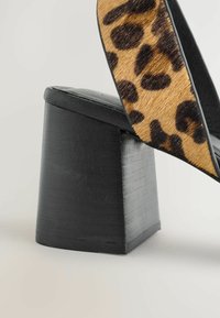 Juodas odinis blokinis kulnas su tekstūruota paviršiumi, viršuje puoštas leopardų rašto paneliu rudų ir juodų atspalvių, sukuriant kontrastingą dizainą.
