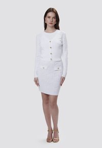 Witte gebreide cardigan en rok set met gouden knopen, voorzien van textuurpatronen. De cardigan heeft een aansluitende snit en lange mouwen.