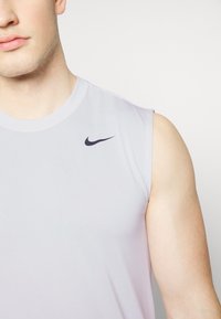 Jasnoszara bezrękawnik sportowy Nike z czarnym logo na lewym ramieniu, gładka faktura tkaniny i okrągły dekolt.