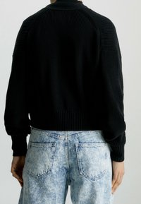 Černý žebrovaný svetr s dlouhými rukávy, kulatým výstřihem a zkráceným lemem, spárovaný se světle modrými džínami s kyselinovým omráčením.