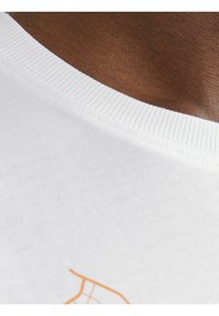 Camiseta de algodón blanca con cuello redondo acanalado y detalle gráfico en color naranja. Vista en primer plano que destaca la textura y el contraste de colores.