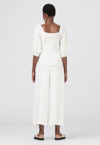 Weißes Oberteil mit Puffärmeln und quadratischem Ausschnitt, kombiniert mit weißen weiten Hosen. Glatte Textur, minimalistisches Design, lässiger Stil.