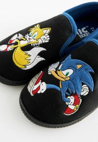 Melnas slaidas čības ar izšūtiem rakstiem, kuros attēloti Sonic un Tails. Zilas akcents, struktūrēta auduma un gumijas zoles.