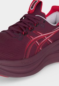 Σκούρο κόκκινο παπούτσι για τρέξιμο Asics με ενισχυμένη σόλα FF Blast+, δεμένα κορδόνια και κόκκινο-λευκό λογότυπο στο πλάι και στη γλώσσα.