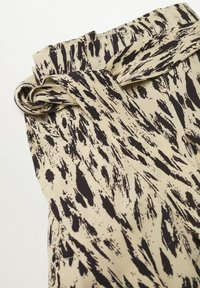 Tissu beige avec des motifs abstraits noirs, doté d'un design froncé et d'un accent noué à la taille. Texture lisse et léger.