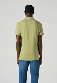 Olivgrön kortärmad polo skjorta, gjord av slät tyg, med klassisk krage och bakre fålldesign. I kombination med blå denimjeans.