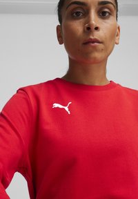 Felpa rossa con scollatura a girocollo, con un logo Puma bianco sul lato sinistro del petto. Realizzata in morbido cotone con polsini a costine.