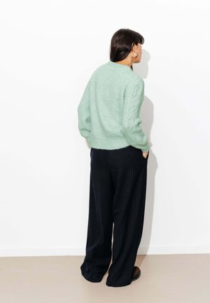 Pull en tricot vert menthe avec ourlet côtelé et détail ajouré sur les manches, associé à un pantalon large rayé bleu marine.