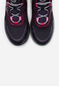 Paire de baskets noires et violettes avec des accents roses et des lacets blancs-noirs à motif sur fond blanc.