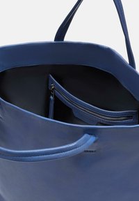 Sac en cuir bleu, présentant une texture lisse, une poche zippée intérieure et des poignées doubles. L'ouverture sur le dessus révèle un compartiment spacieux.