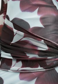 Κοντινή λήψη ραμμένου υφάσματος με λευκή βάση και σκούρο κόκκινο λουλουδένιο σχέδιο σε εφαρμοστό ένδυμα.