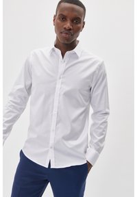 Witte lange mouw button-up shirt gemaakt van gladde stof, met een klassieke kraag en een rechte snit, gedragen met blauwe broek.