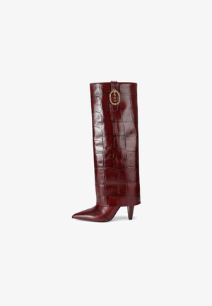 Botte montante en cuir synthétique crocodile bordeaux avec un bout pointu et un talon aiguille. Dotée d'éléments décoratifs en métal doré en haut.