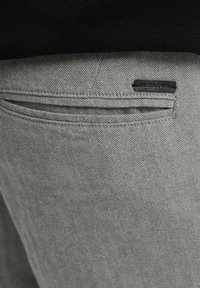 Sive herringbone hlače s teksturiranim uzorkom, s crnom tkaninom oznakom "JACK & JONES" i glatkim, ravnim dizajnom džepova.