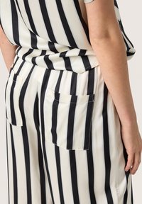 Pantaloni a gamba larga in tessuto leggero, con strisce verticali bianche e nere, due tasche posteriori e un design rilassato.
