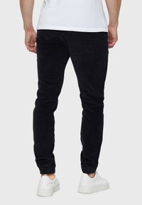 Pantalons en velours côtelé noirs avec une coupe ajustée, présentant une texture côtelée, un design de jambe fuselée, et accompagnés de baskets blanches.