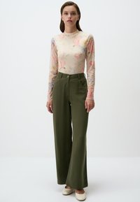 Blusa floreale trasparente a maniche lunghe in colori pastello abbinata a pantaloni larghi a vita alta verde oliva e scarpe color crema.