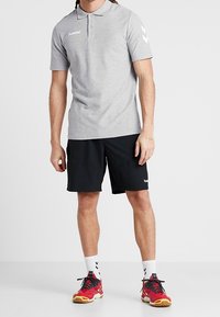 Polo gris avec col et trois boutons, associé à un short de sport noir. Baskets rouges avec des accents jaunes et chaussettes blanches.