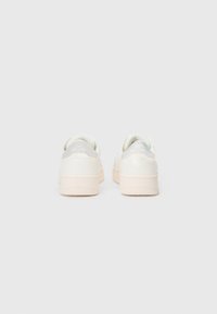 Adidași albi cu un finisaj din piele netedă, talpă de cauciuc bej deschis și accente irizate la călcâi. Design minimalist cu forme rotunjite.