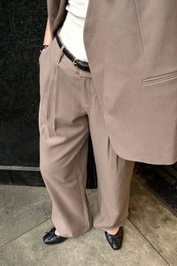 Beige, pleated trousers with a relaxed fit, paired with a white top and a black belt. Black flats with bows complete the outfit.