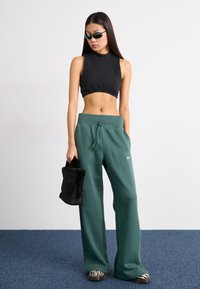 Grønne joggebukser med snor i livet og Nike-logo, sammen med en ribbet svart crop-top, dyreprint tøfler, og en svart pelskoffert.