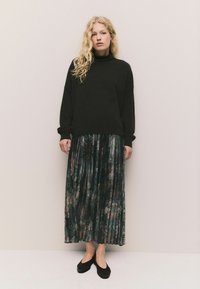 Schwarzer oversized Pullover, gefalteter langer Rock mit einem dunklen Blumenmuster und schwarzen flachen Schuhen. Strukturiertes Material, lockere Passform.