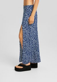 Marinblå maxikjol med sidoklyv; lätt och flödande tyg med vita blommönster. Bärs med svarta platåsandaler.