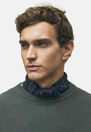 Marine paisley tørklæde båret over en tekstureret olivengrøn trøje. Tørklædet har indviklede mønstre og blødt stof; trøjen har et ribbet design.