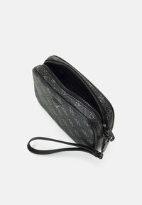 Plic negru cu fermoar, cu un model monogram subtil. Dispune de un brâu detașabil pentru încheietura mâinii și o textură netedă, elegantă.