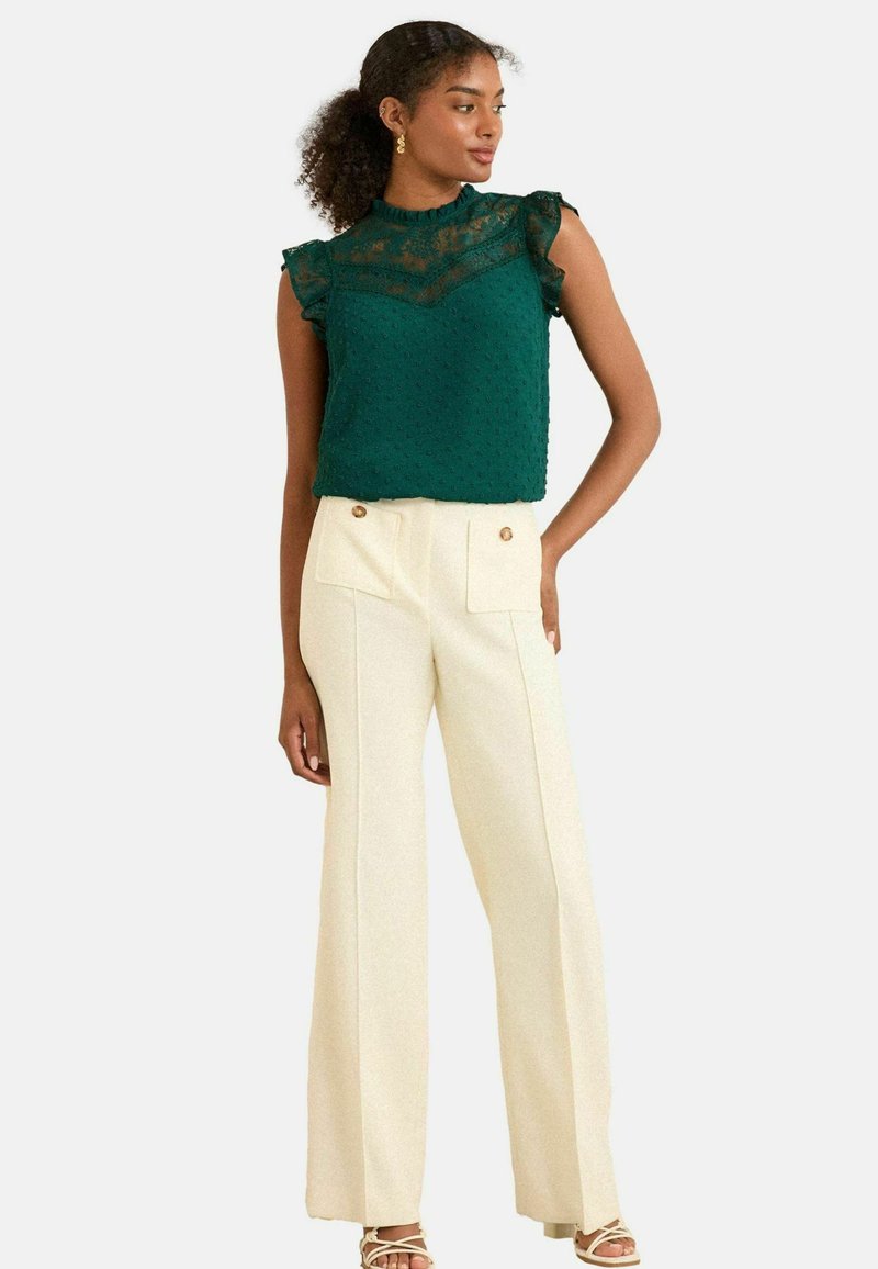 Grön texturerad blus med spetsöverlägg, volangärmar, som matchas med krämfärgade vida byxor med framfickor och guldknappar.