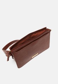 Pochette marron à motif crocodile avec une fermeture zippée, quincaillerie dorée et une sangle de poignet réglable. Intérieur doublé dans un tissu assorti.