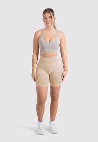 Jasnoszary sportowy biustonosz z regulowanymi ramiączkami i marszczonym detalem z przodu, zestawiony z beżowymi szortami z wysokim stanem, oba wykonane z elastycznego materiału.